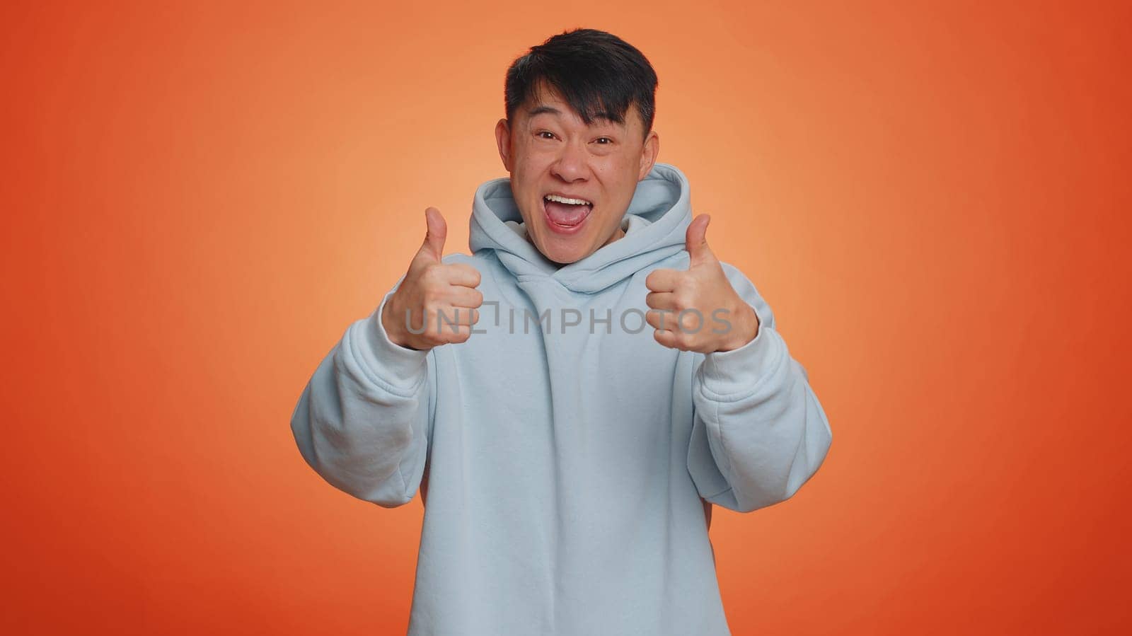 Nice, good job. Asian handsome businessman man showing thumbs up and nodding in approval, enjoy successful great work. Adult guy isolated alone on orange studio background. People lifestyle concept