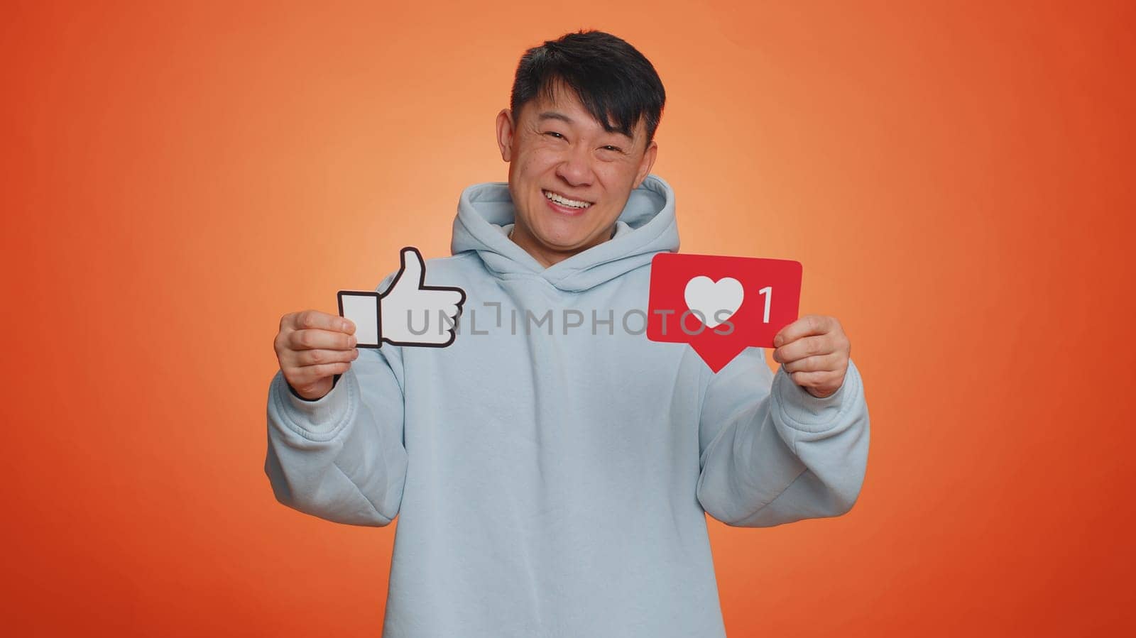 Like. Happy asian man raises inscription thumbs up banner thumbs up agrees with something, gives positive reply recommends advertisement likes good on social media. Guy on orange studio background