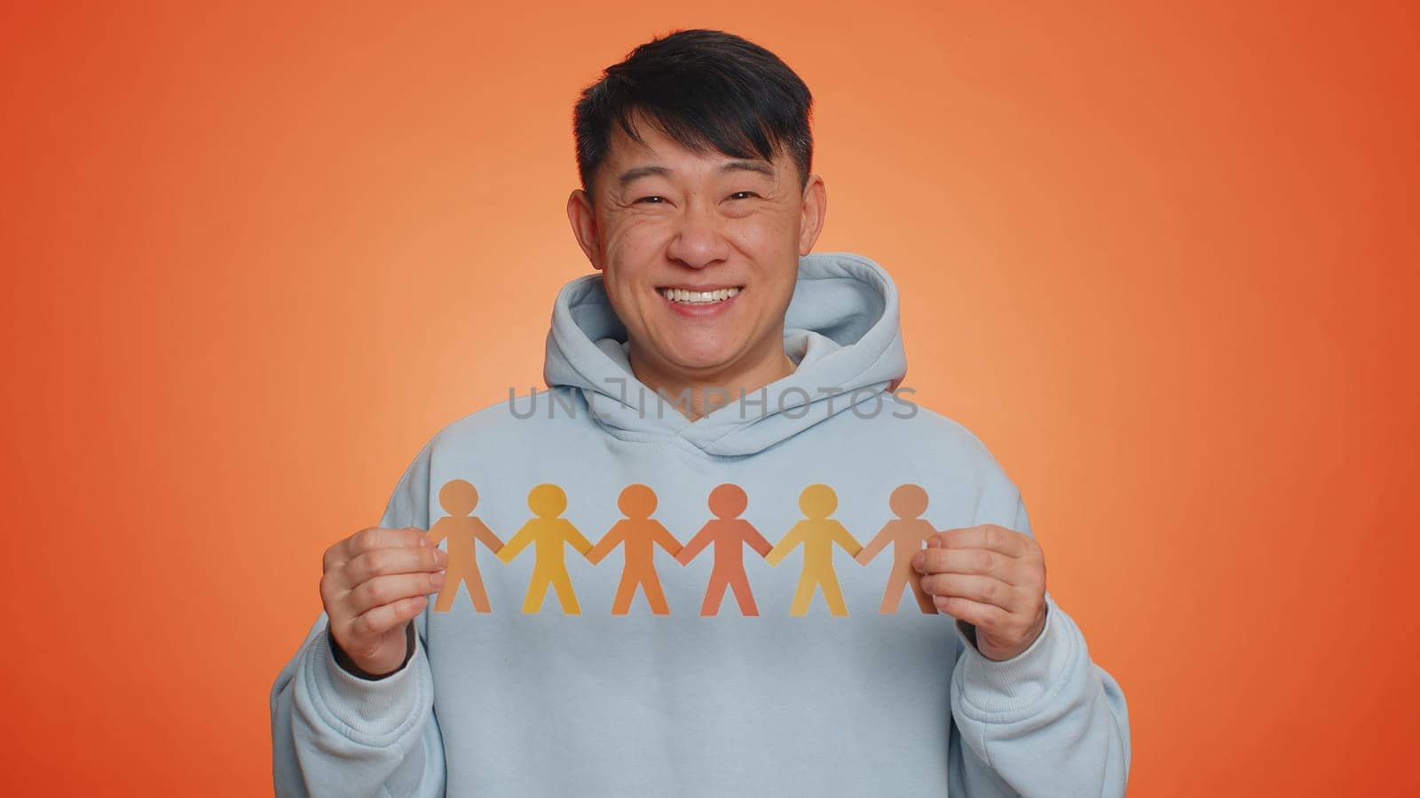 Man showing multiracial different skin color human shape cut out of paper, concept of teamwork, partnership, community, unity, people support love against racism. Asian guy on orange studio background