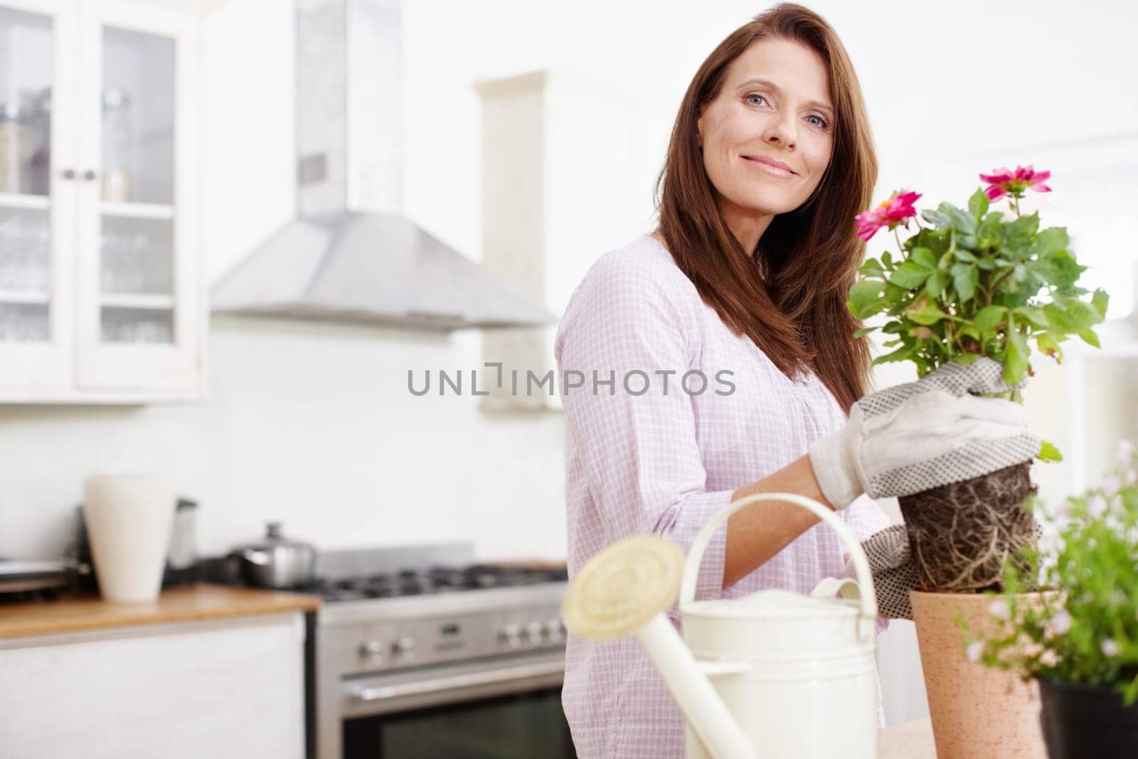 Brightening up her home with some summer plants. Portrait of a beautiful woman potting some plants for summer. by YuriArcurs