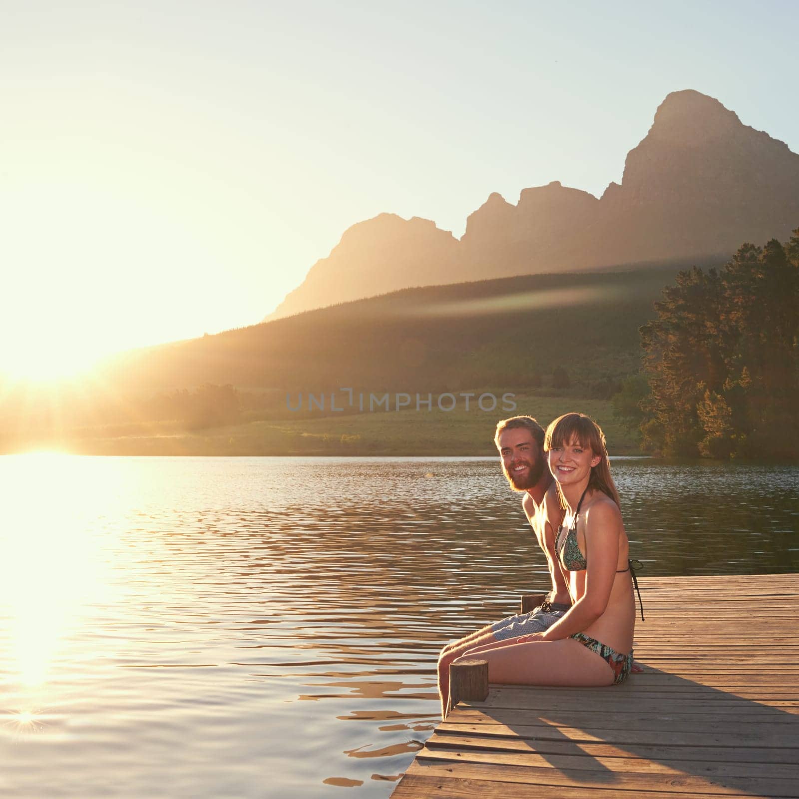 Enjoying a perfect day in paradise. an affectionate young couple in swimsuits sitting on a dock at sunset. by YuriArcurs