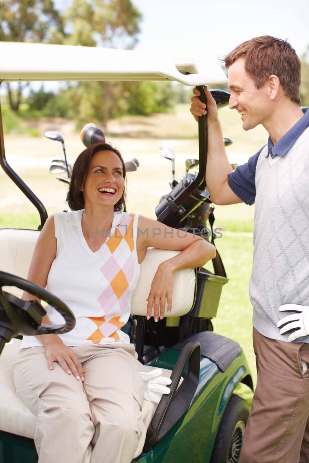 Love and laughter on the green. Smiling woman seated in a golf cart with her husband standing alongside her. by YuriArcurs