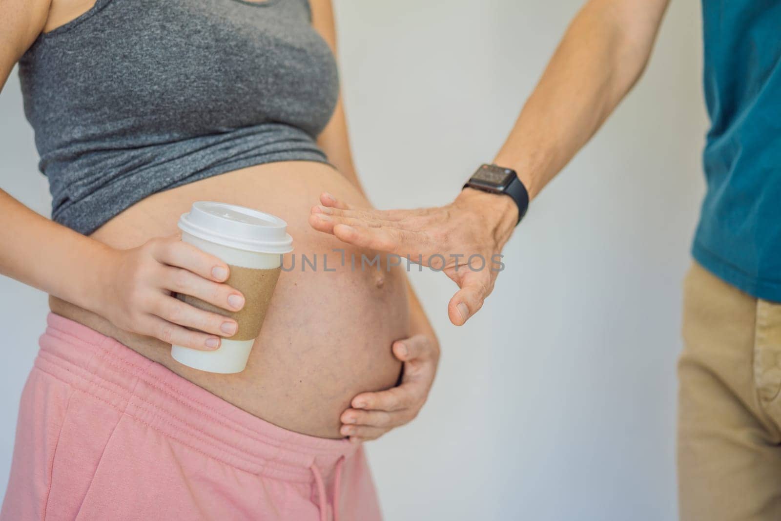 Husband forbids pregnant wife to drink coffee. A pregnant woman holds a cup of coffee in her hands. Caffeine safety, myths about coffee during pregnancy concept.