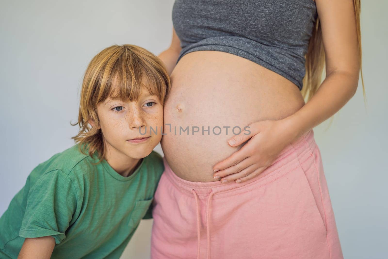 Young beautiful pregnant woman and eldest son. The cute boy leaned his ear against his mother's belly. Expecting a baby in the family concept. Preparing an older child for a younger one.