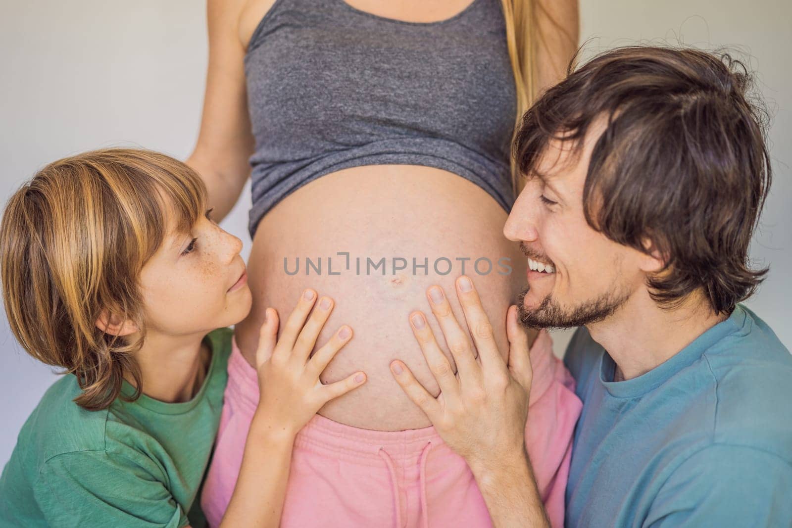 Father and elder son listen to mom's pregnant belly.
