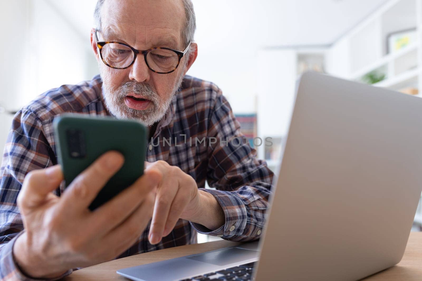 Mature adult caucasian man using phone at home office. by Hoverstock