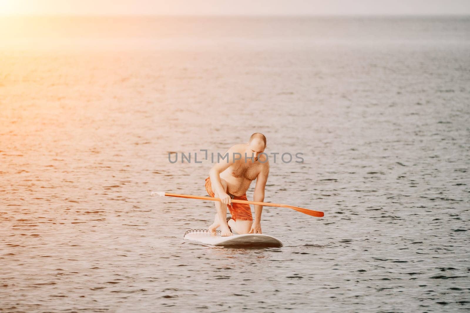 Active mature male paddler with his paddleboard and paddle on a sea at summer. Happy senior man stands with a SUP board. Stand up paddle boarding - outdor active recreation in nature. by panophotograph