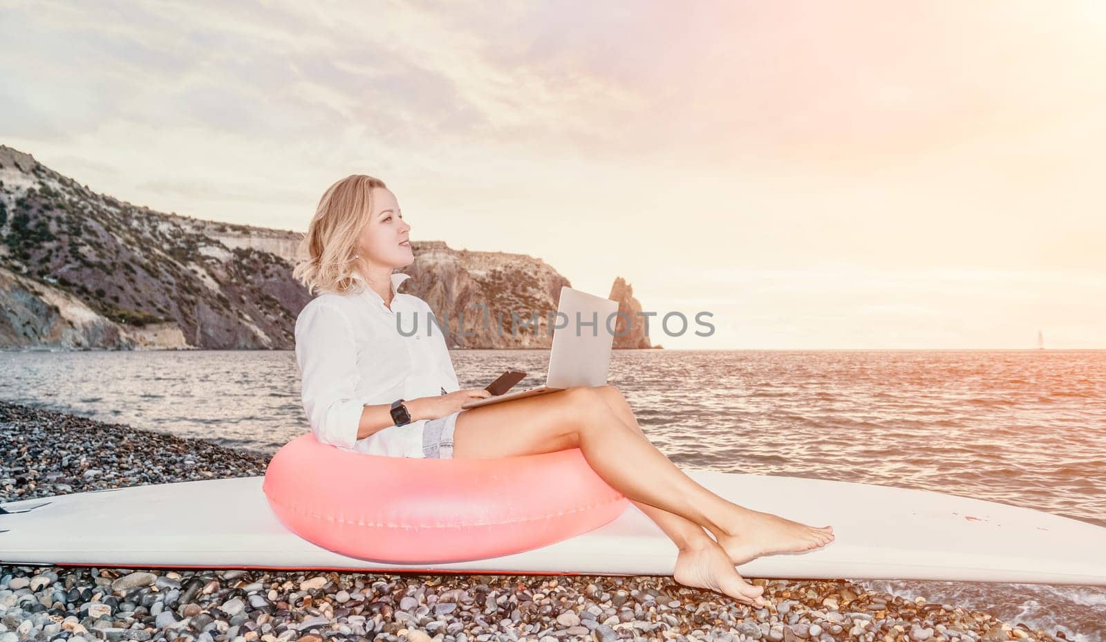 Digital nomad, Business woman working on laptop by the sea. Pretty lady typing on computer by the sea at sunset, makes a business transaction online from a distance. Freelance, remote work on vacation by panophotograph