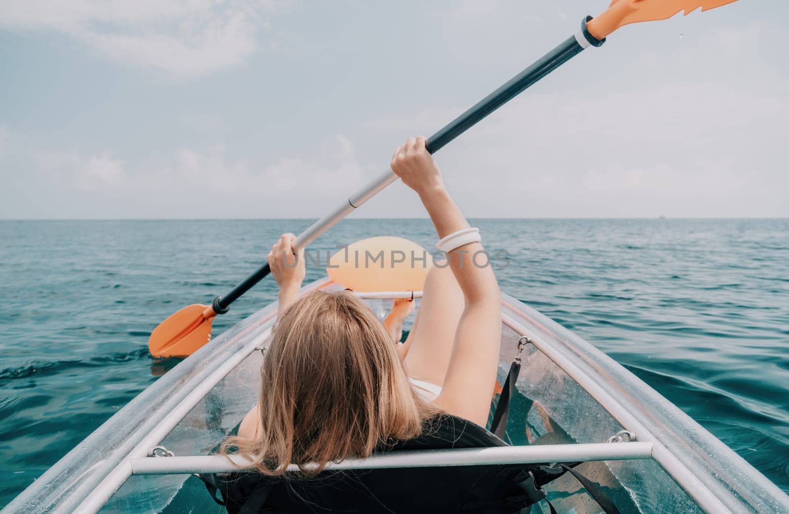 Woman in kayak back view. Happy young woman with long hair floating in transparent kayak on the crystal clear sea. Summer holiday vacation and cheerful female people relaxing having fun on the boat by panophotograph