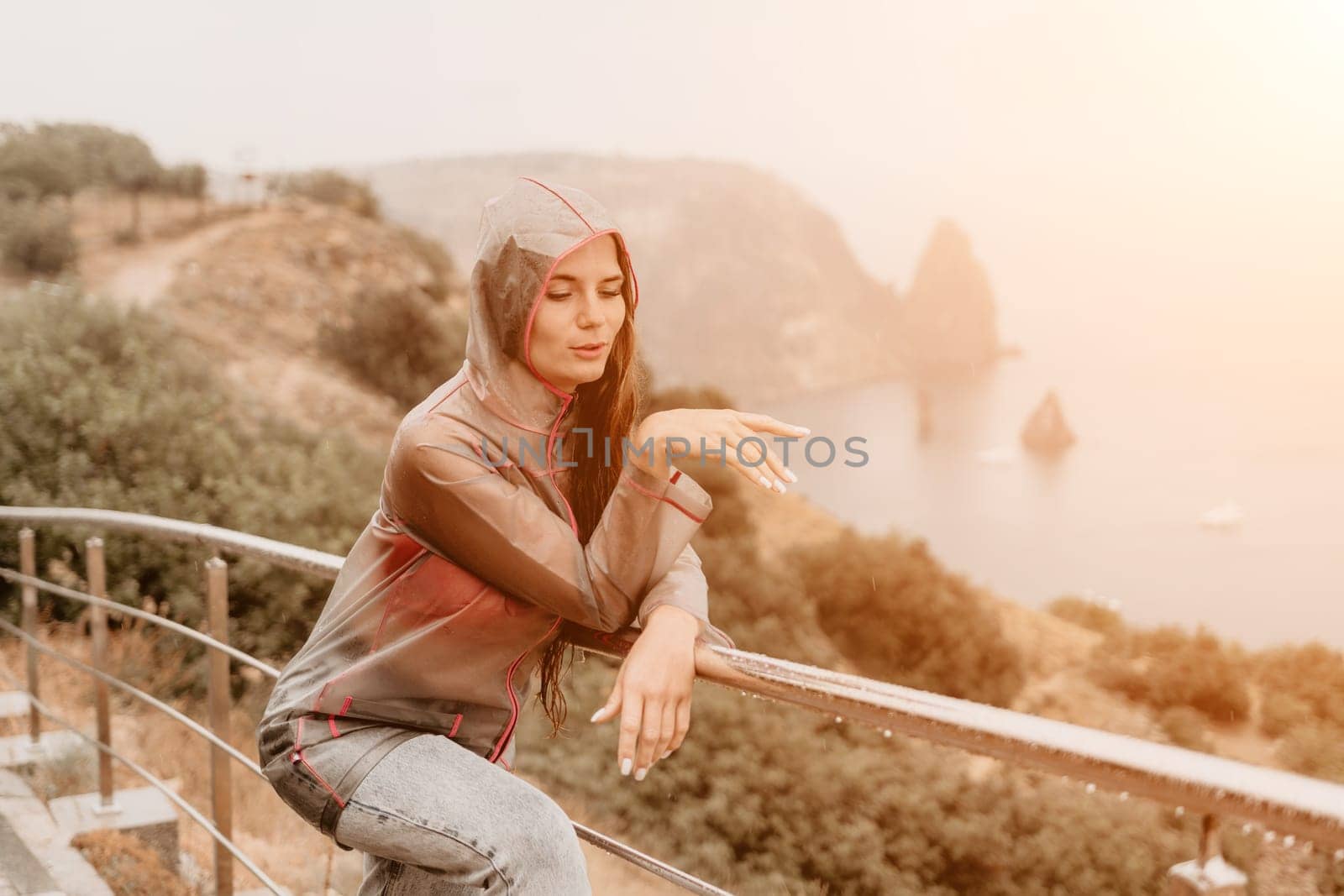 Woman rain umbrella. Happy woman portrait wearing a raincoat with transparent umbrella outdoors on rainy day in park near sea. Girl on the nature on rainy overcast day. by panophotograph