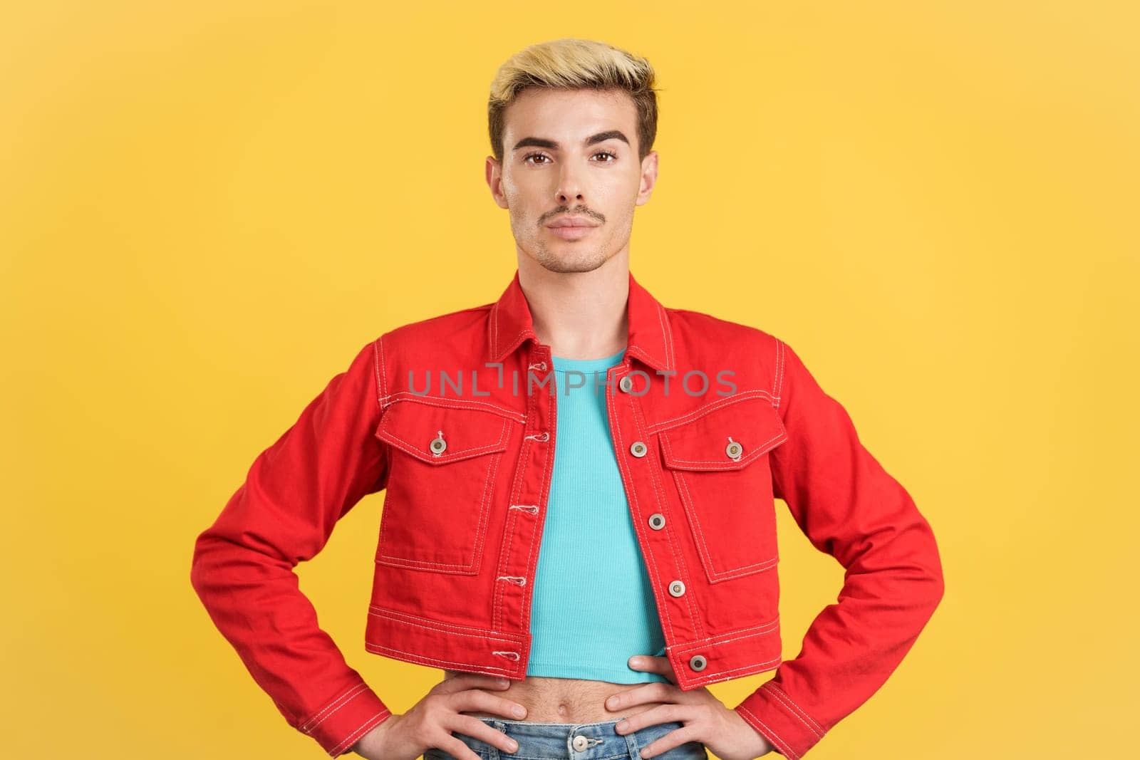 Gay man in colorful clothes looking at camera in studio with yellow background