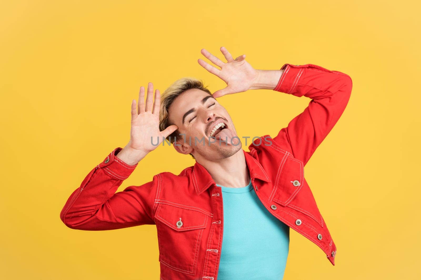 Gay man grimacing and joking with tongue out in studio with yellow background