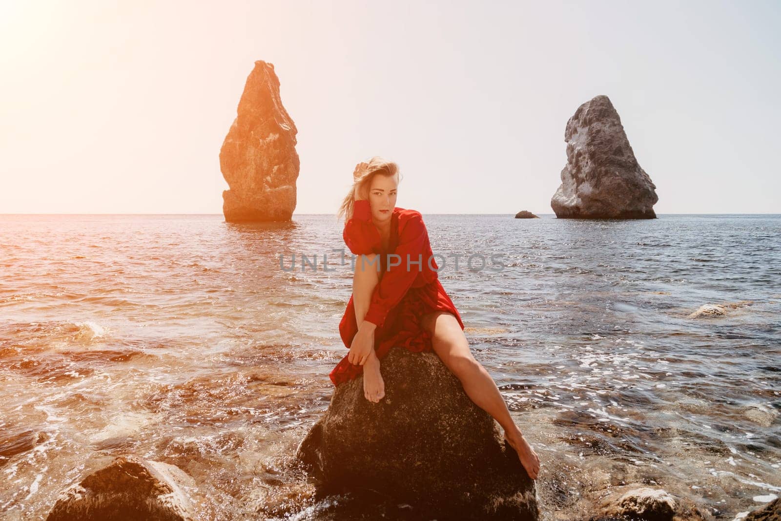 Woman travel sea. Young Happy woman in a long red dress posing on a beach near the sea on background of volcanic rocks, like in Iceland, sharing travel adventure journey