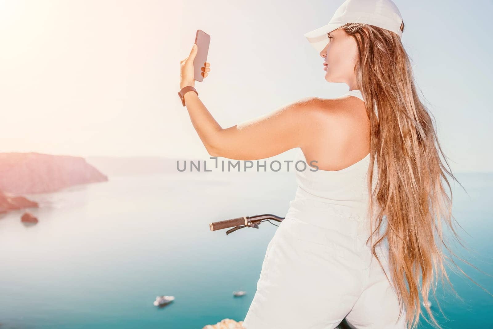 A woman cyclist on a mountain bike looking at the landscape of mountains and sea. Rear view of cyclist woman standing in front to the sea with outstretched arms. Freedom and healthy lifestyle concept. by panophotograph