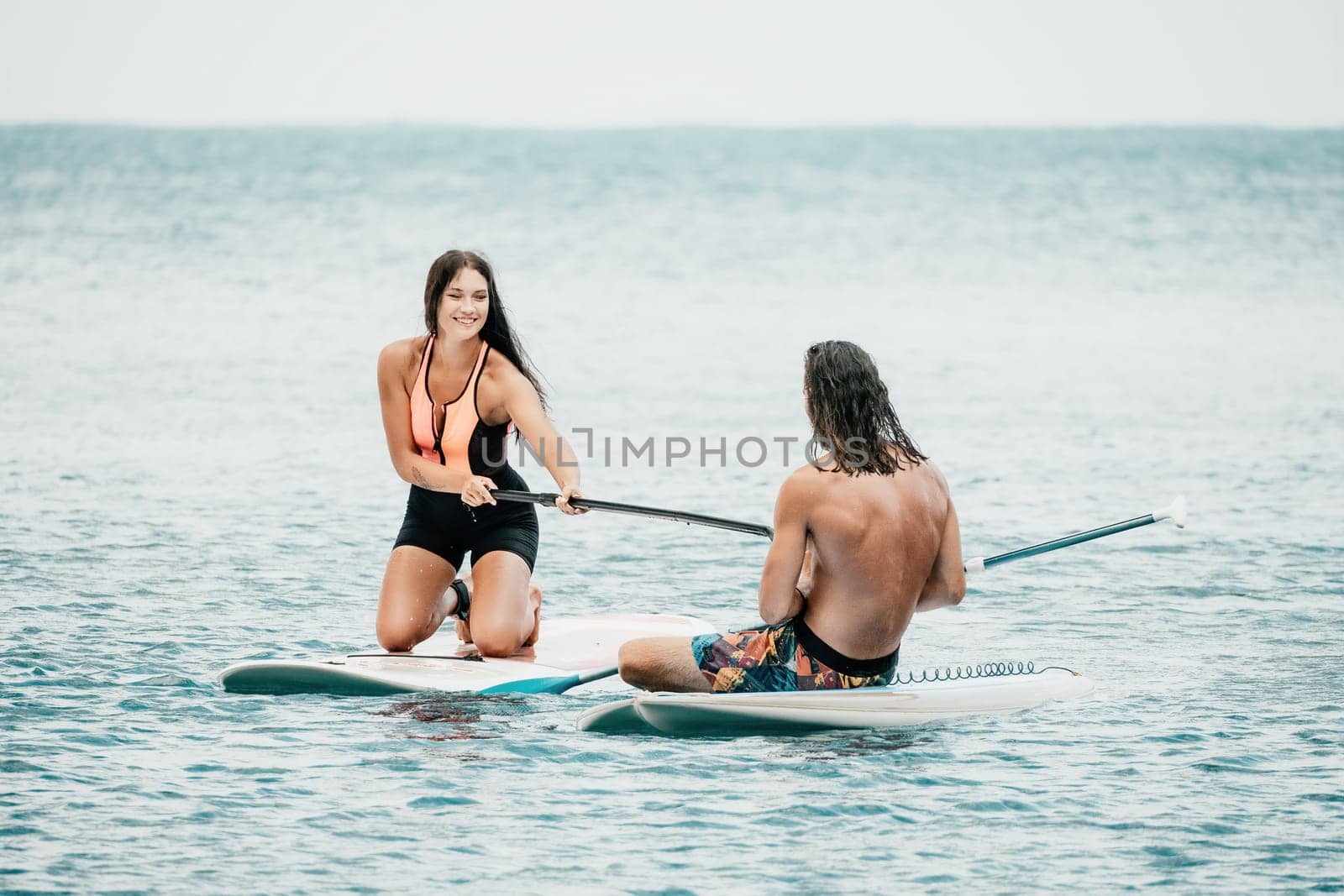 Sea woman and man on sup. Silhouette of happy young woman and man, surfing on SUP board, confident paddling through water surface. Idyllic sunset. Active lifestyle at sea or river