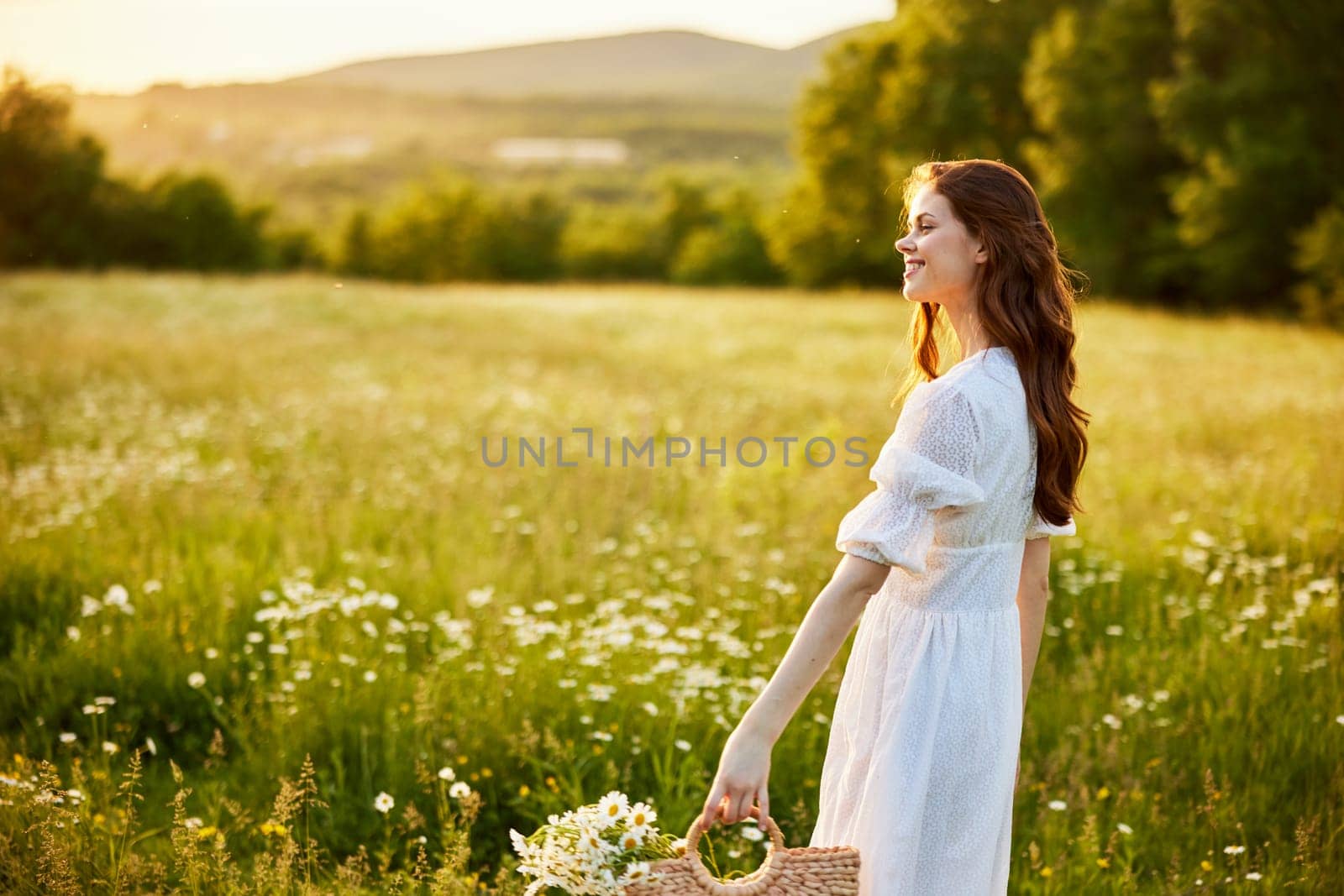 happy woman in a light dress and a wicker basket full of daisies enjoys nature walking in the field. High quality photo