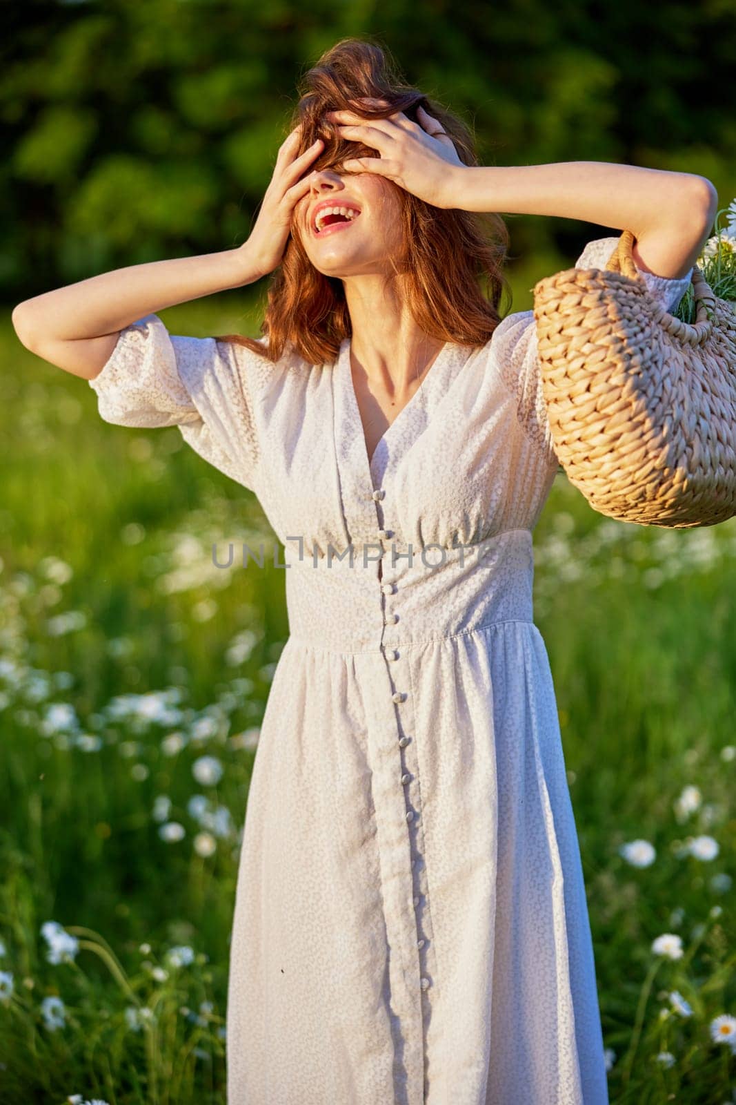 a happy red-haired woman in a light dress stands in a field and covers her face with her hair. High quality photo