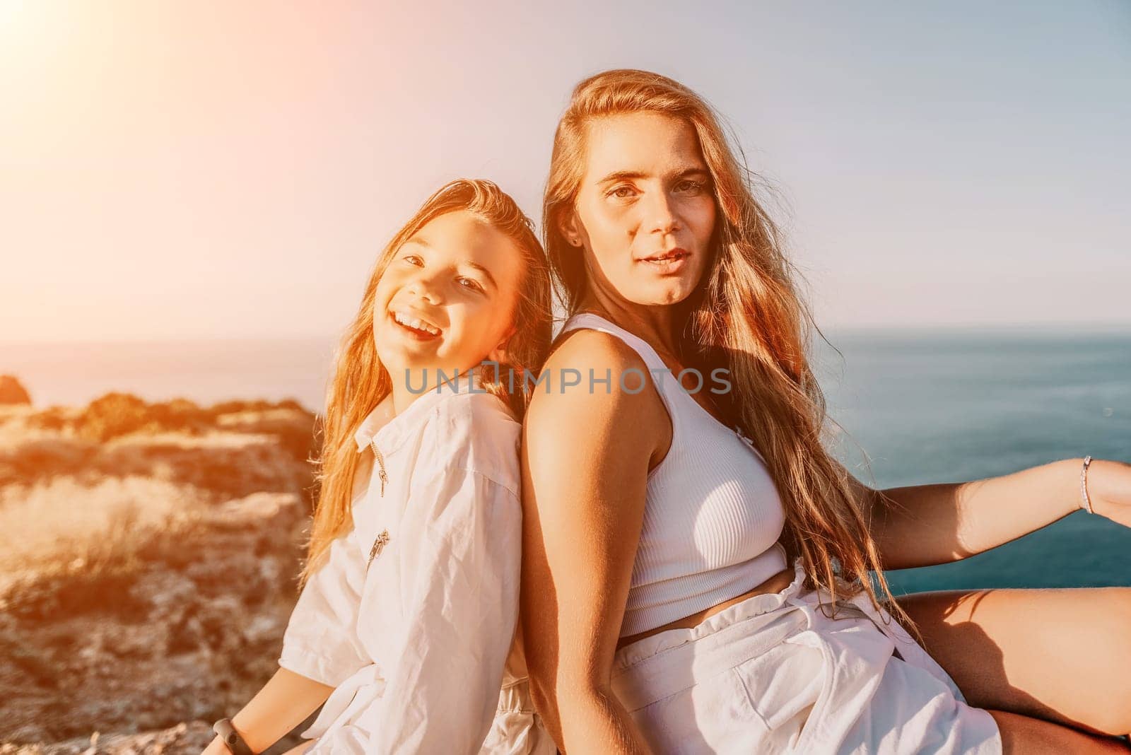 Close up portrait of mom and her teenage daughter hugging and smiling together over sunset sea view. Beautiful woman relaxing with her child.