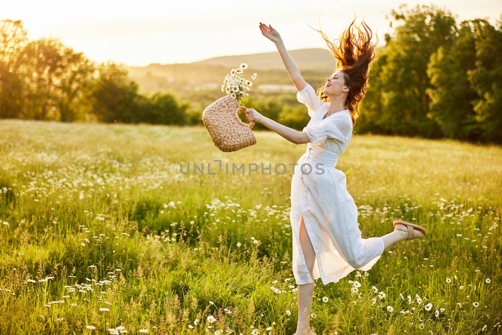 a woman in a light, long dress jumps in a field with a basket of daisies in her hands by Vichizh