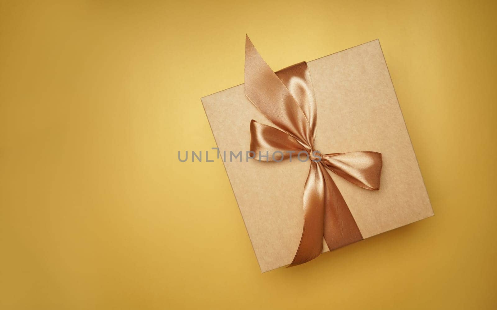 Square gift box. craft paper, yellow color bow knot, ribbons. paper background. empty label, sticker for text. Happy New Year package. top view by aprilphoto