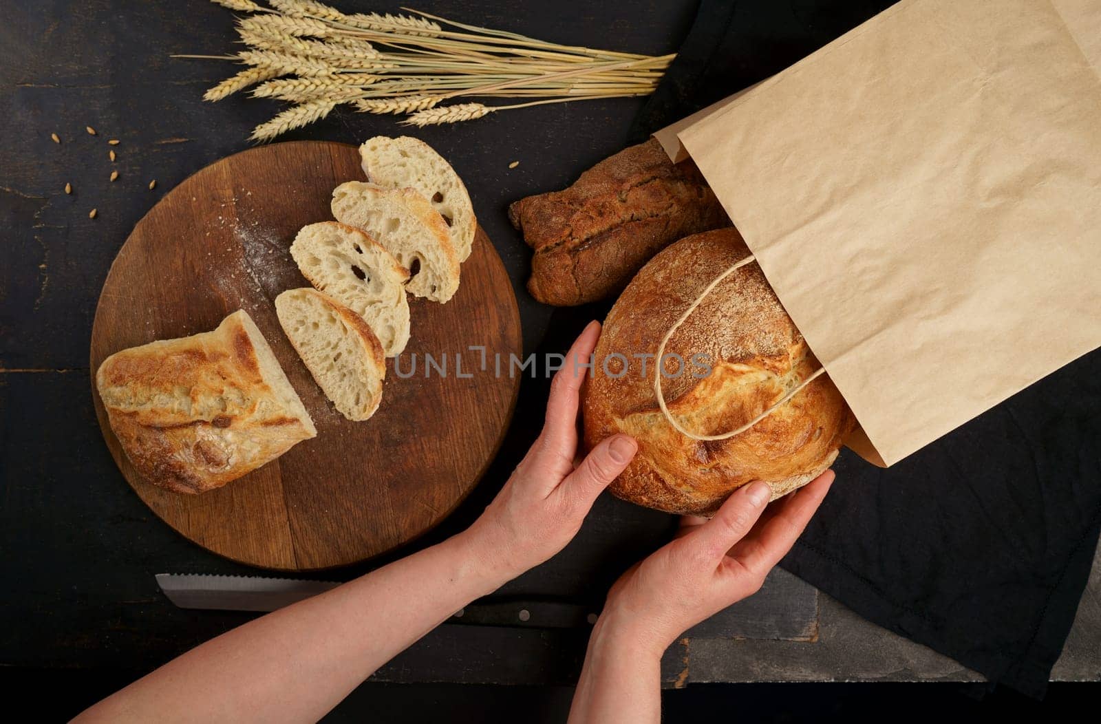 Whole grain bread put on kitchen wood plate with knife for cut. Fresh bread on table close-up. Fresh bread on the kitchen table. The healthy eating and traditional bakery concept. Top viev.