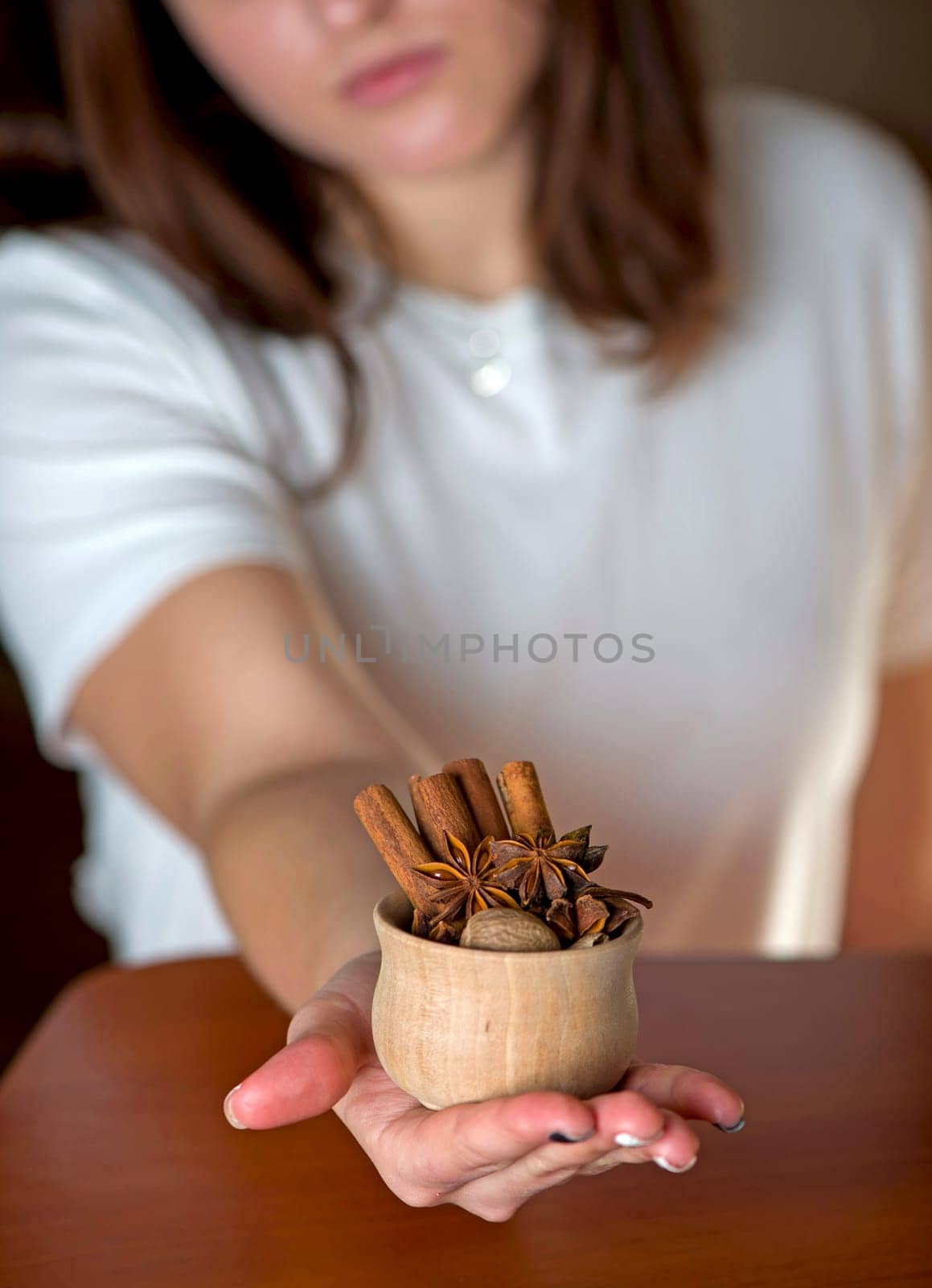 Hands of young woman holding wooden cup with spicesselective focus.