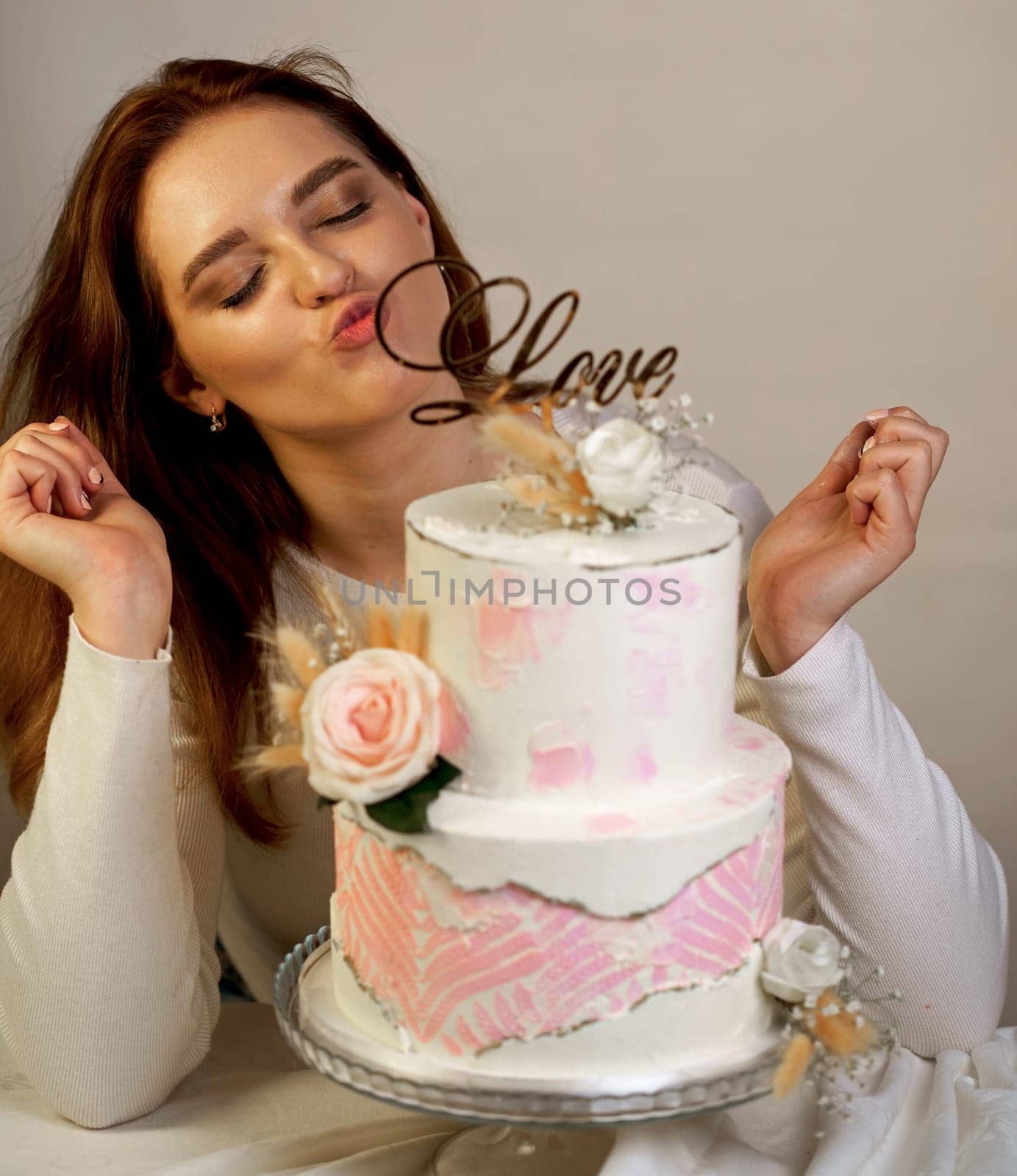 A beautiful girl confectioner shows a cooked two-tiered wedding cake decorated with fresh flowers. by aprilphoto