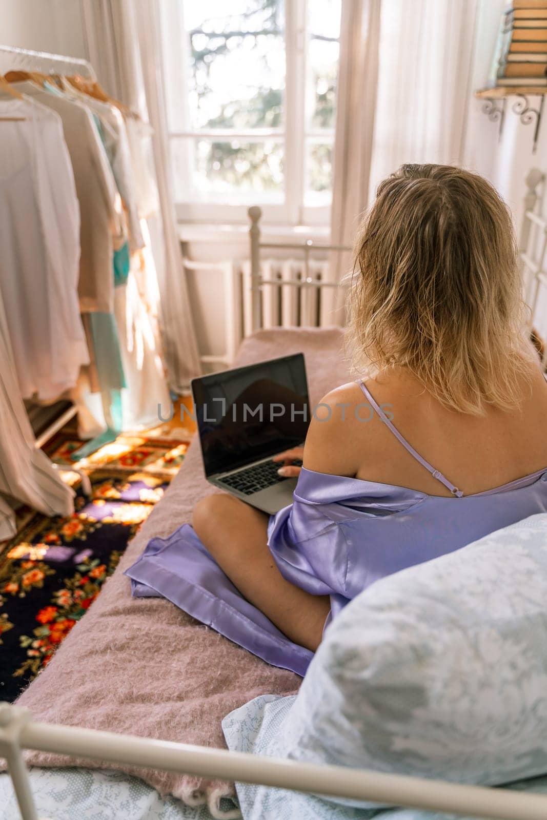 A top view of a woman in a purple nightgown using a laptop on a bed, suggesting that she is working or studying from the comfort of her own home