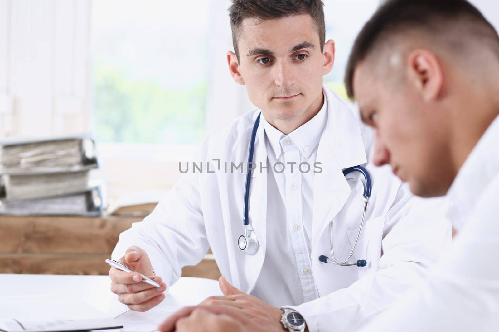 Handsome male medicine doctor with clipboard pad in hands examine patient and prescribe remedy. Exam visitor reception disease prevention ward round visit check 911 healthy lifestyle concept