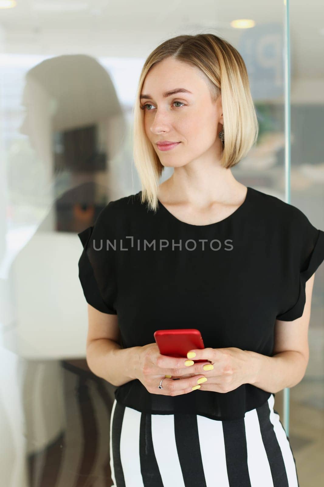 Business woman holding a smartphone in her hands reflection in the glass of red color is trying to call while working break the blonde