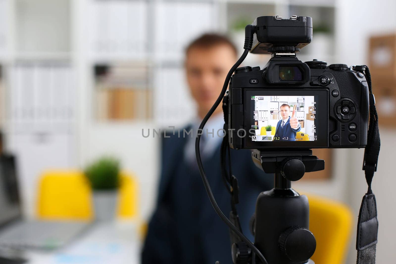 Male in suit and tie show confirm sign arm making promo videoblog or photo session in office camcorder to tripod closeup. Vlogger promotion selfie solution or finance advisor management information