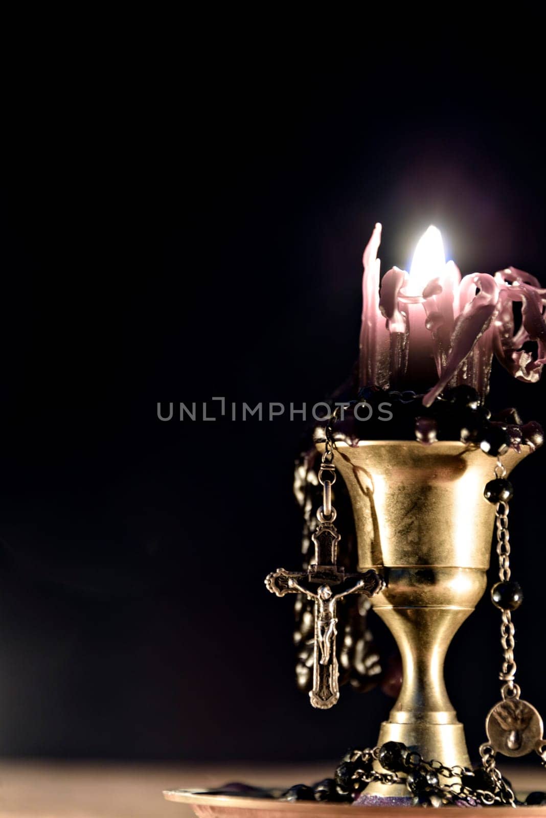 Black candle with rosary on black background