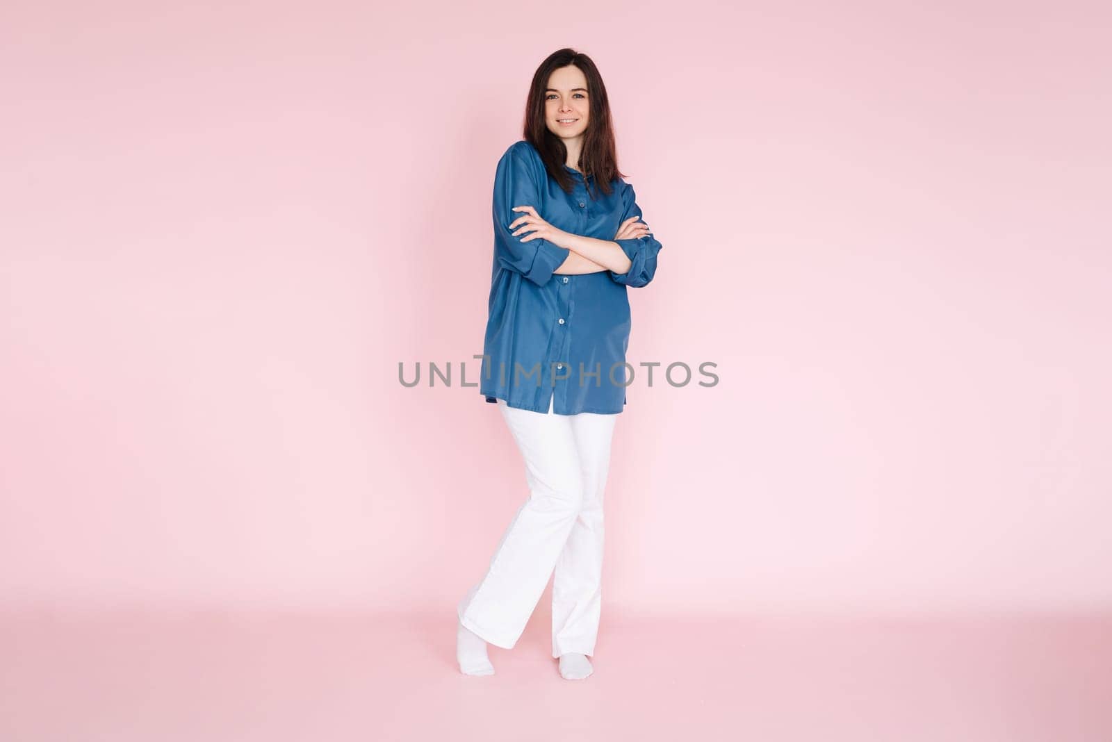 Confident businesswoman in smart casual attire standing with folded hands in front of pink background - Full body shot for professional profile or website banner