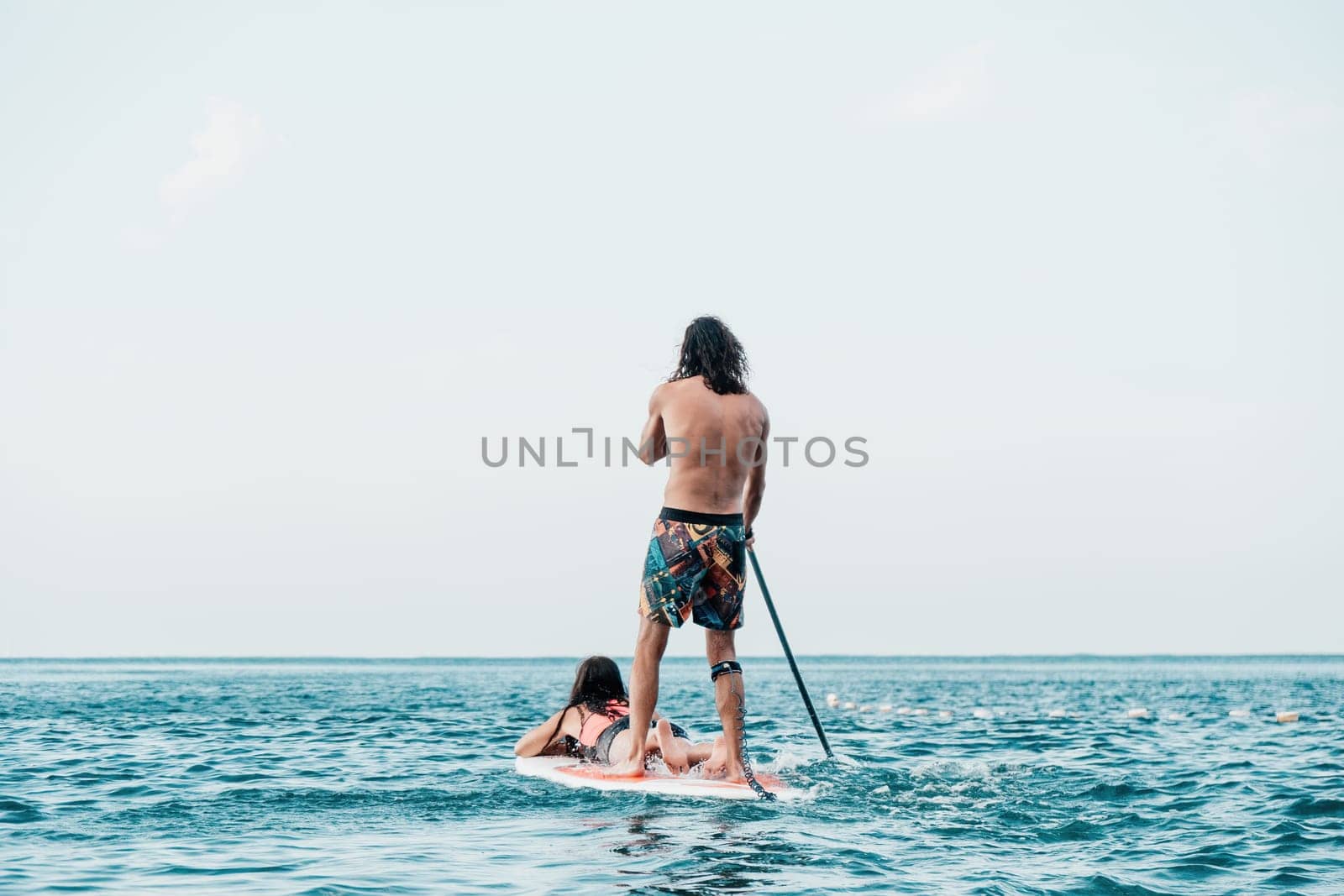 Silhouette of woman standing, surfing on SUP board, confident paddling through water surface. Idyllic sunset or sunrise. Sports active lifestyle at sea or river.