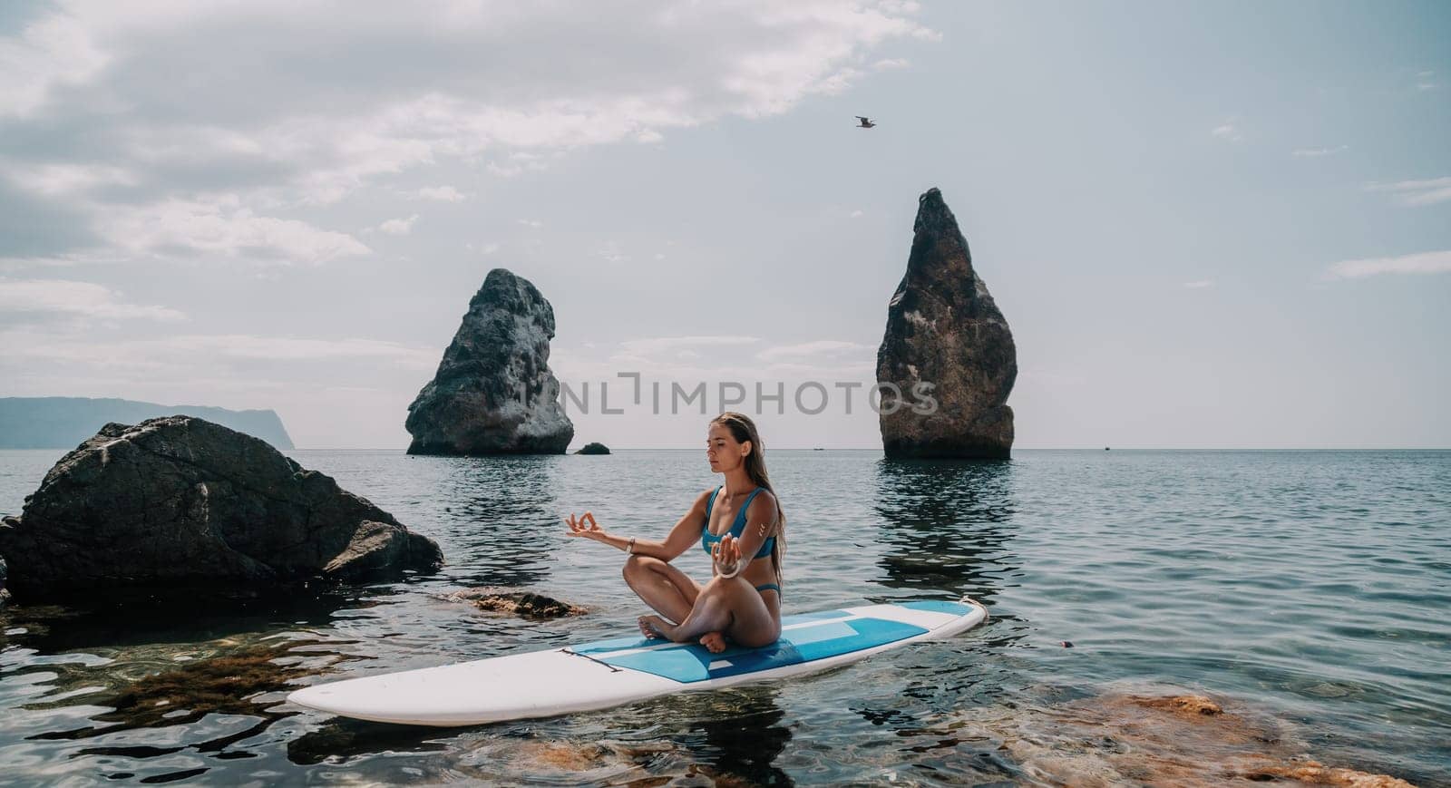 Woman sup yoga. Middle age sporty woman practising yoga pilates on paddle sup surfboard. Female stretching doing workout on sea water. Modern individual hipster outdoor summer sport activity