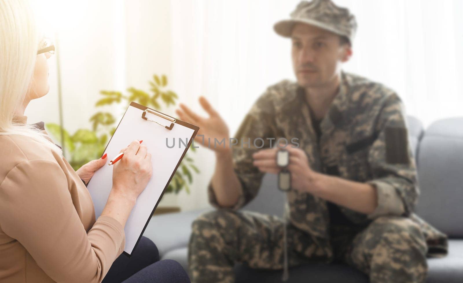 sad soldier with ptsd talking at psychiatrist and gesturing while sitting on couch during therapy session.