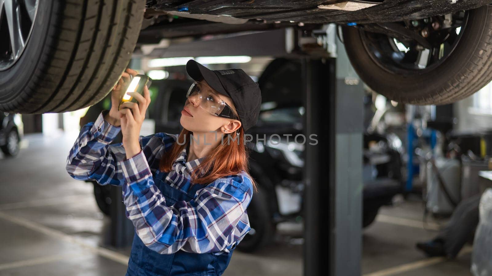 A female mechanic inspects a lifted car. A girl at a man's work. by mrwed54