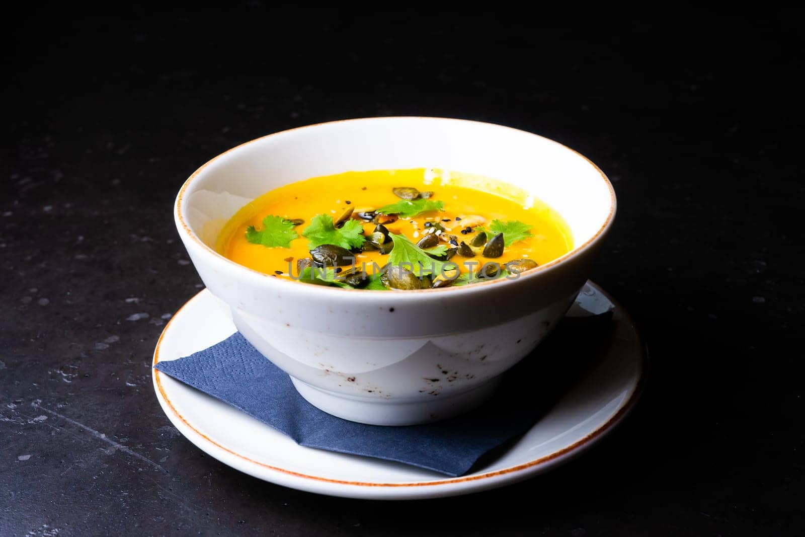 Pumpkin cream soup with parsley on gray stone and wooden background. Top view, copy space by Zelenin