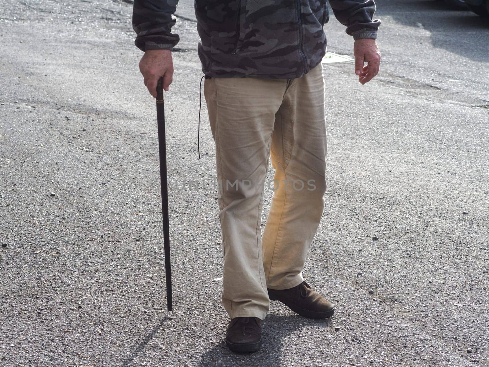 Macro shot of elderly unrecognizable man holding the wooden handle of a wppd walking cane, outdoors in the street