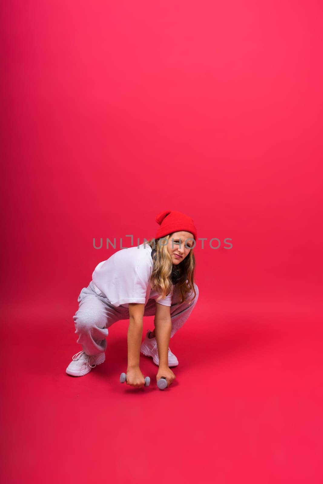 Kid girl doing fitness exercises with dumbbells on red background by Zelenin