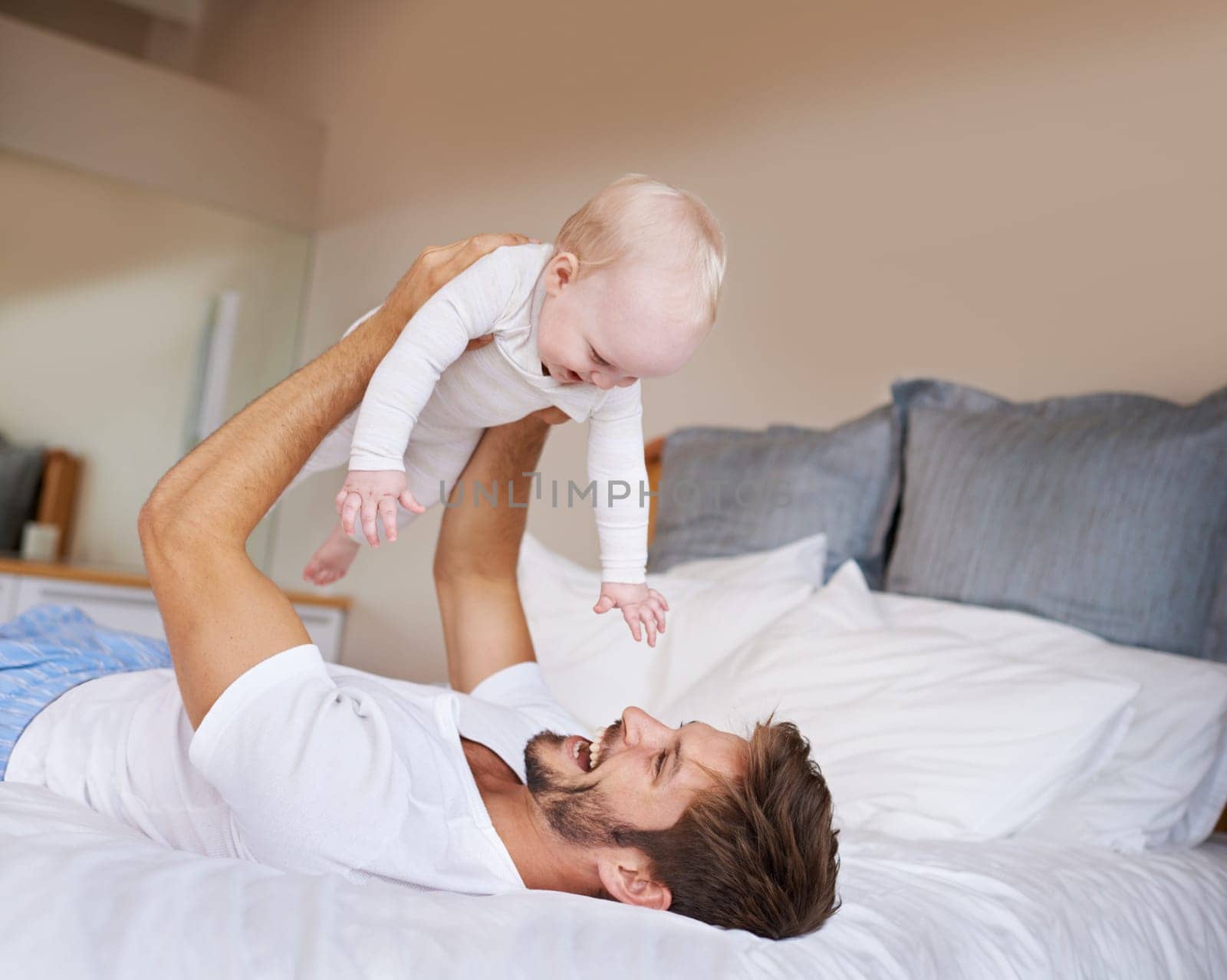 Safe in daddys hands. a father lying on a bed holding his baby girl up in the air. by YuriArcurs