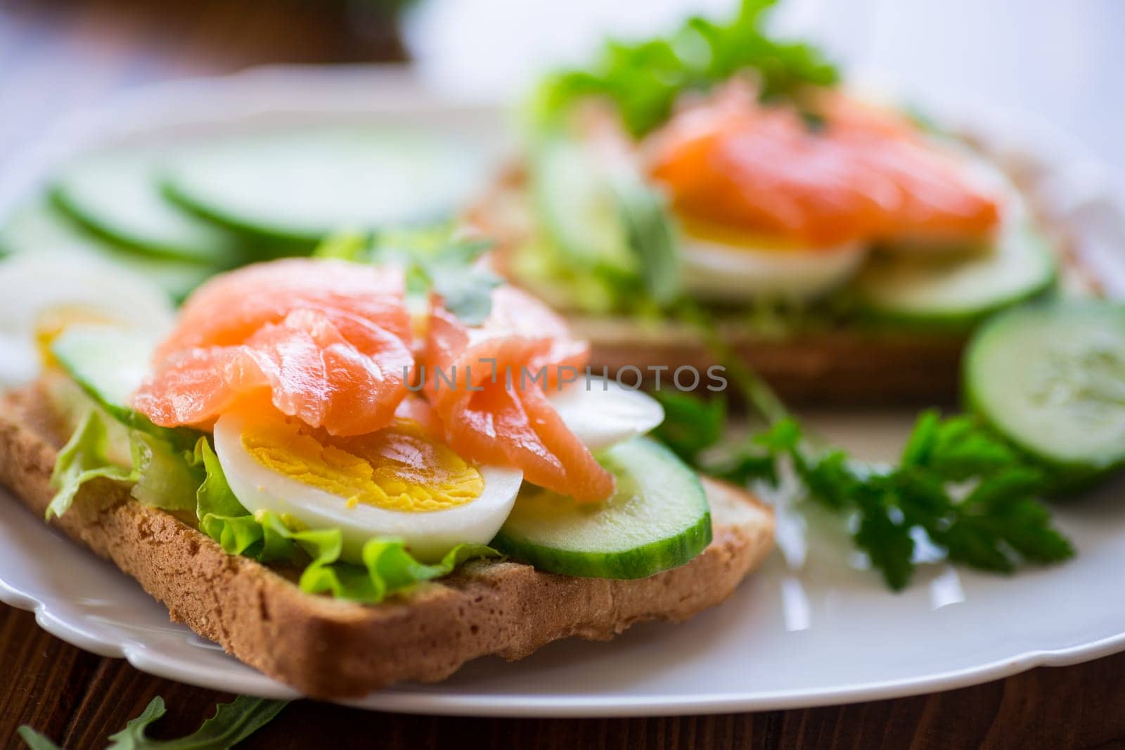 fried toast with lettuce, egg, cucumbers and red fish in a plate, on a wooden table.