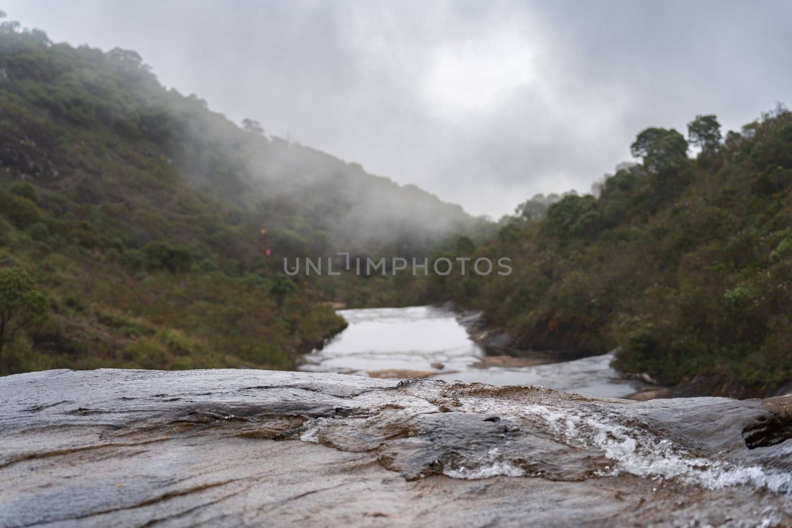 A mystical misty waterfall edge with a green jungle backdrop and flowing water down below.