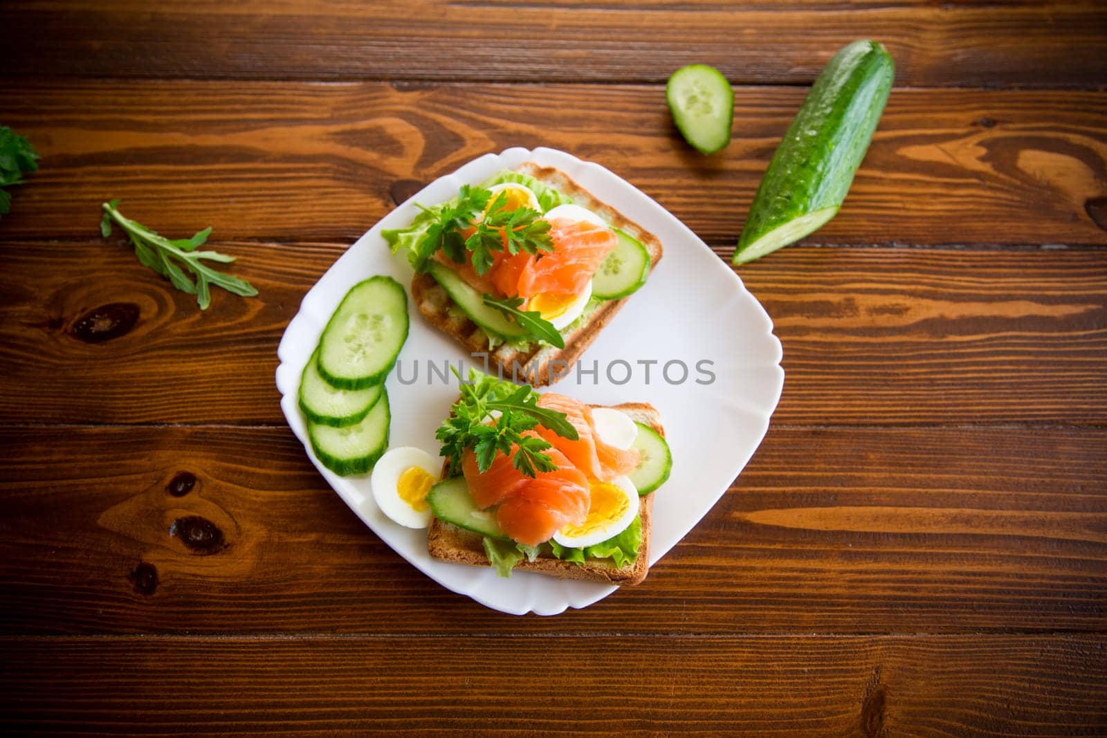 fried toast with lettuce, egg, cucumbers and red fish in a plate, on a wooden table.