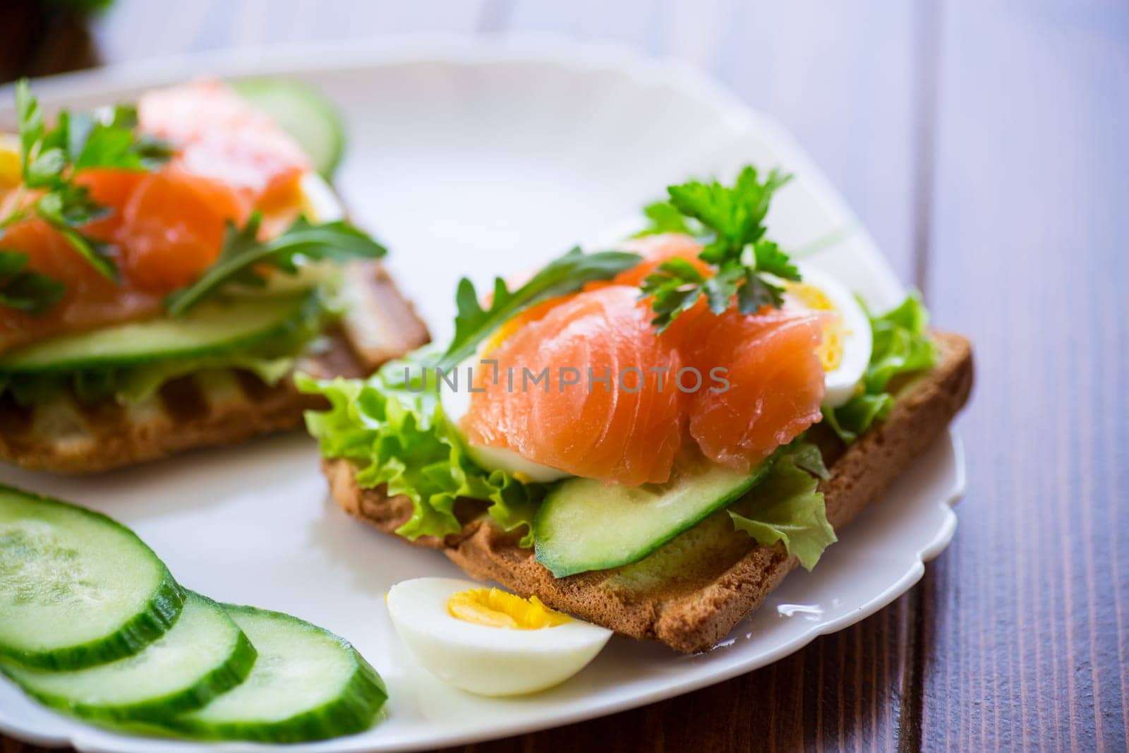 fried toast with lettuce, egg, cucumbers and red fish in a plate, on a wooden table.