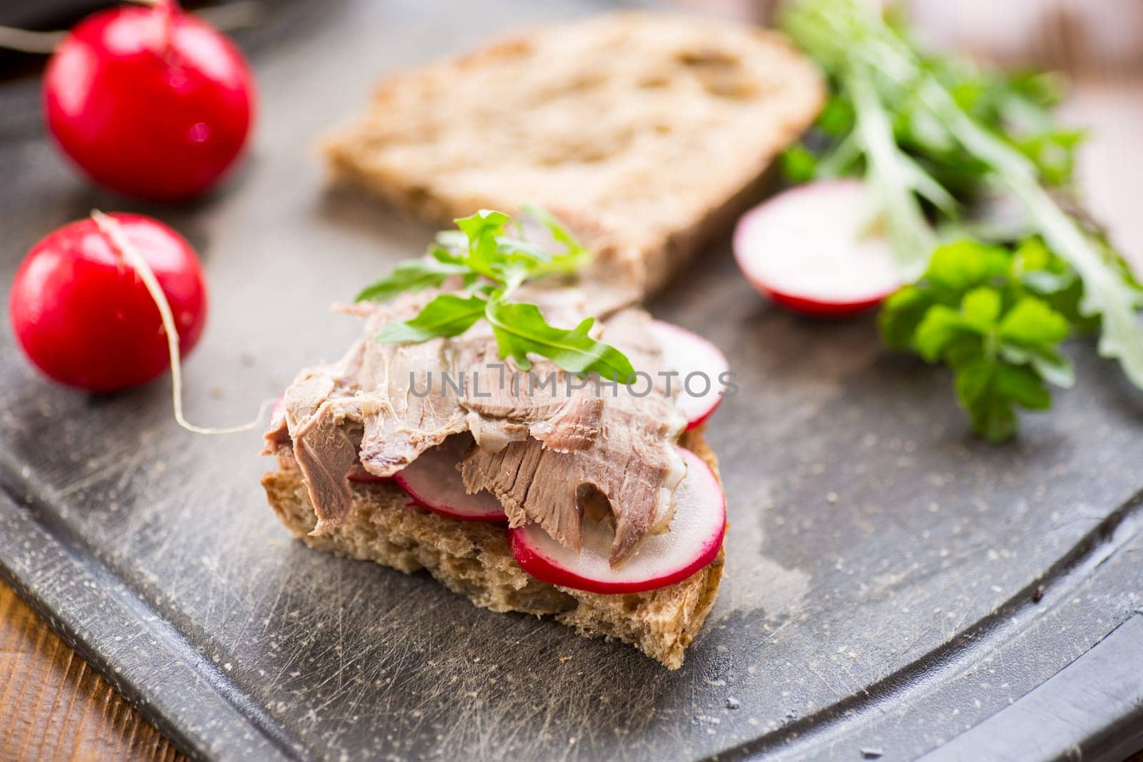 sandwich with baked meat, radish and herbs on a wooden table.