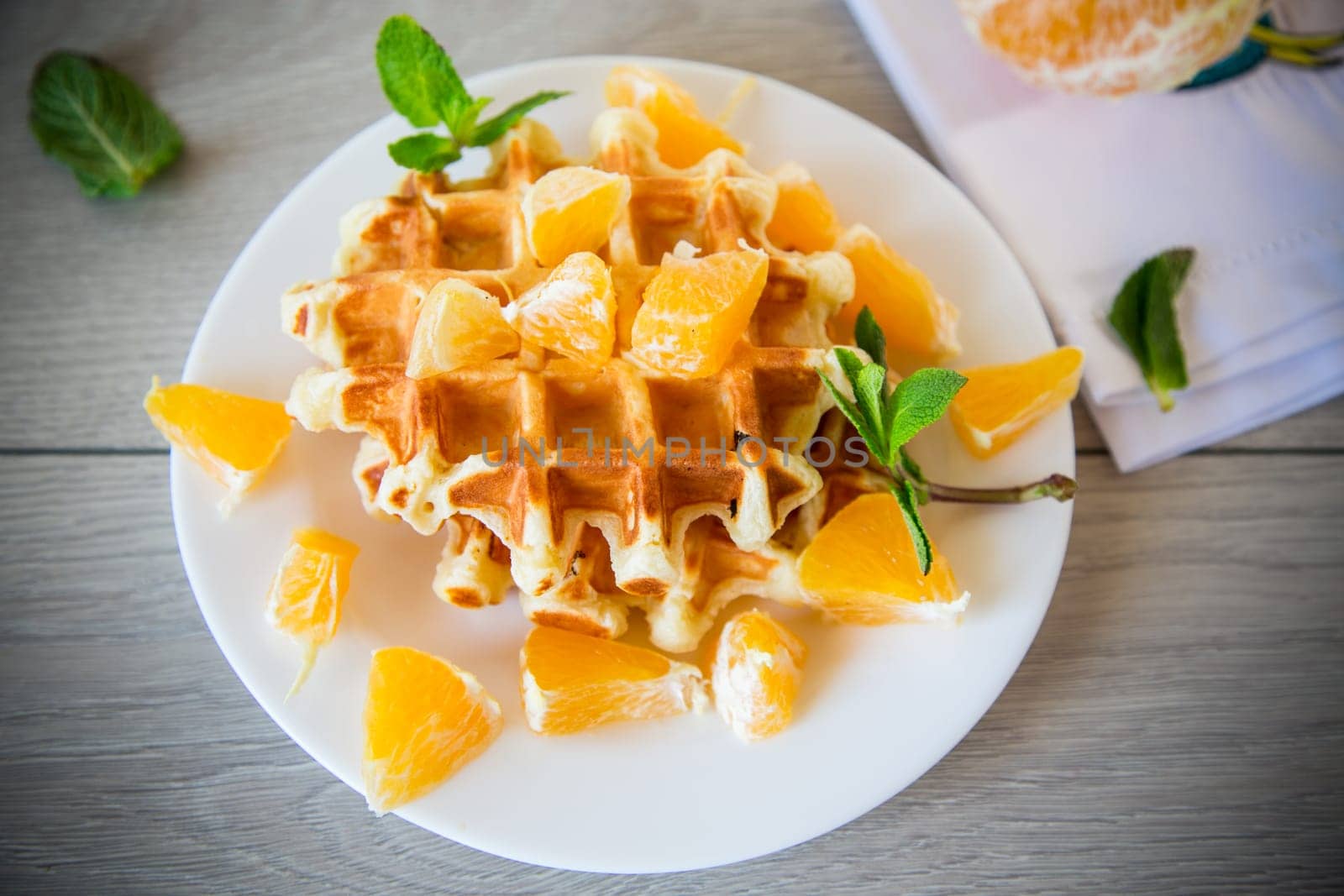 Cooked sweet Belgian waffles with oranges on a wooden table.
