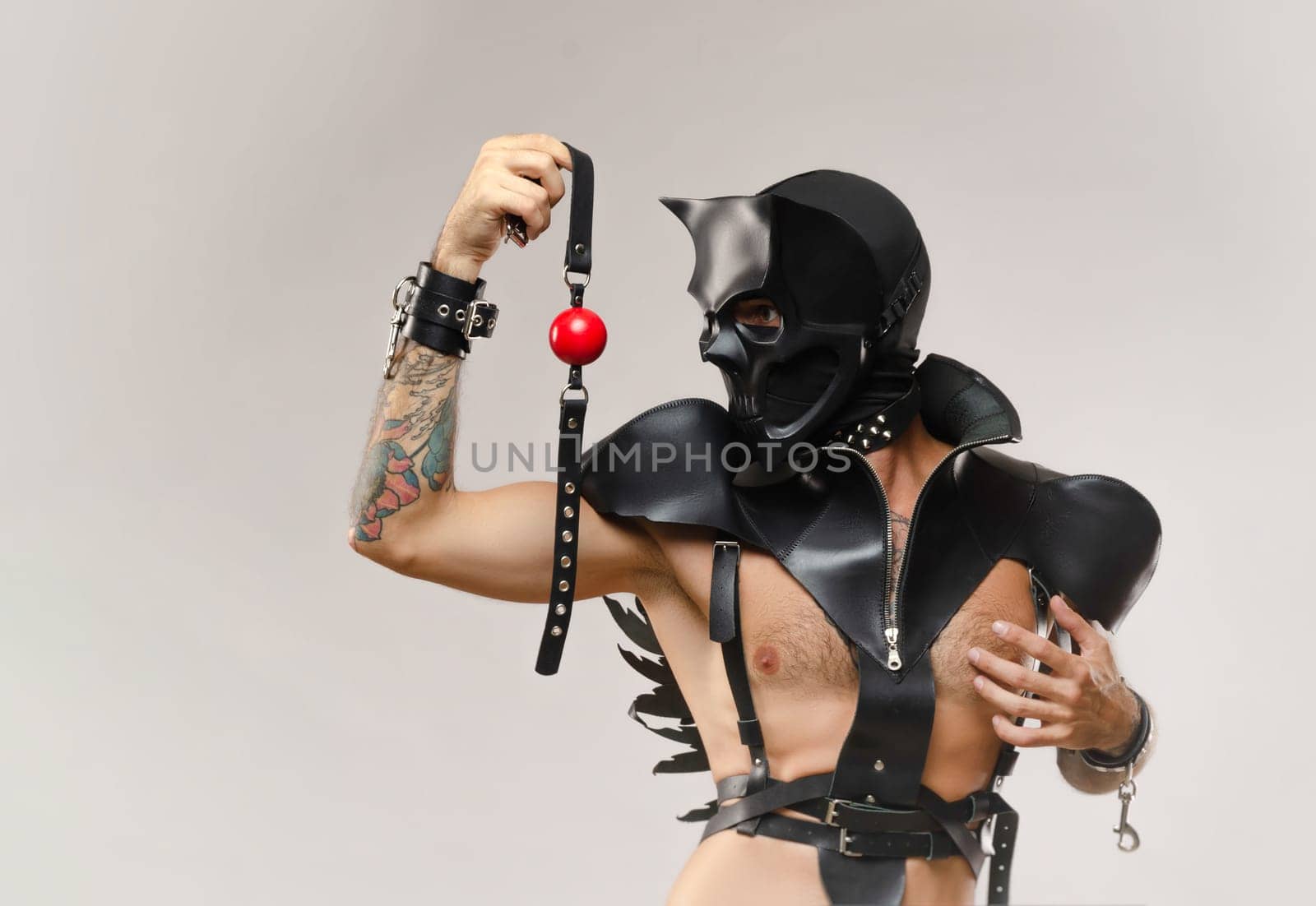sexy a man in a bdsm skull mask, dressed in a leather raincoat with leather handcuffs and straps on the body on a light background of a copy paste by Rotozey