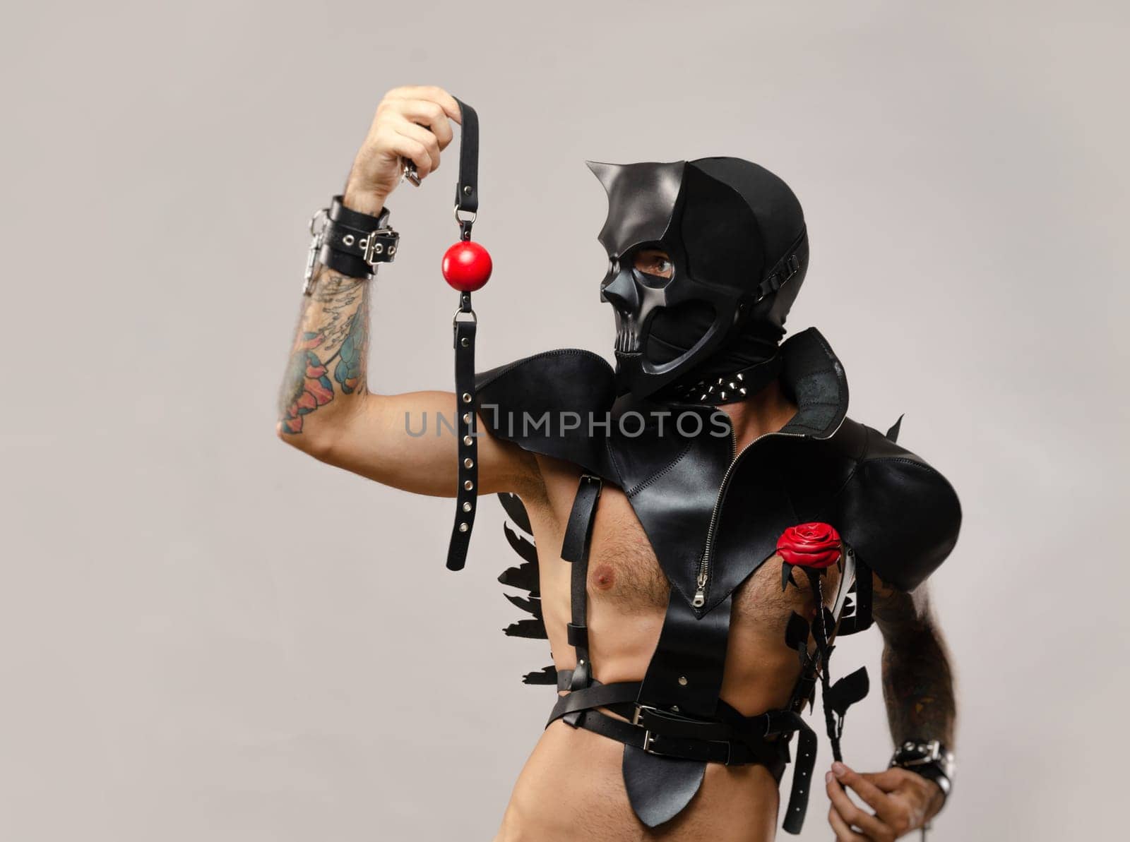 sexy a man in a bdsm skull mask, dressed in a leather raincoat with leather handcuffs and straps on the body on a light background of a copy paste by Rotozey