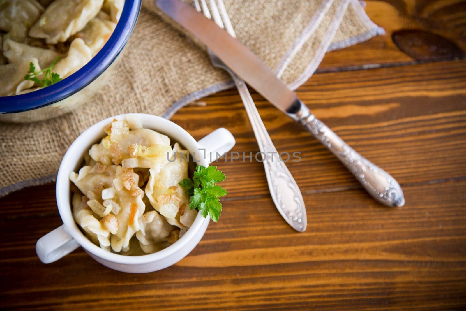 cooked dumplings with potatoes and fried onions, in a bowl on a wooden table.